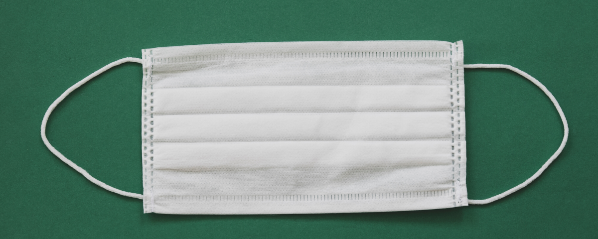 White surgical mask lying flat on a green background.