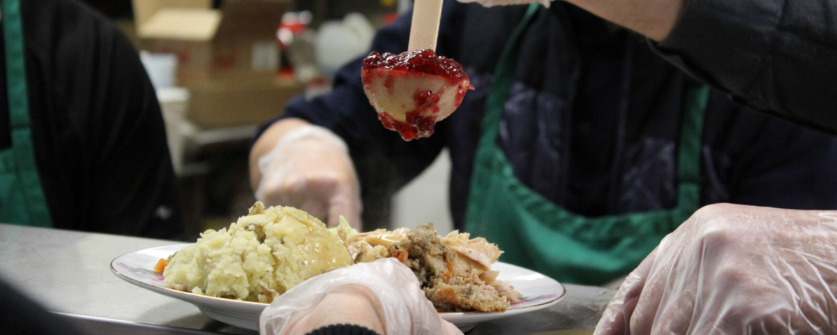 Close up of a Christmas dinner with stuffing and cranberry sauce being served by a person wearing a Mission Services green apron.