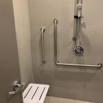 A tiled shower stall with accessible grab bar, seating, and shower head.