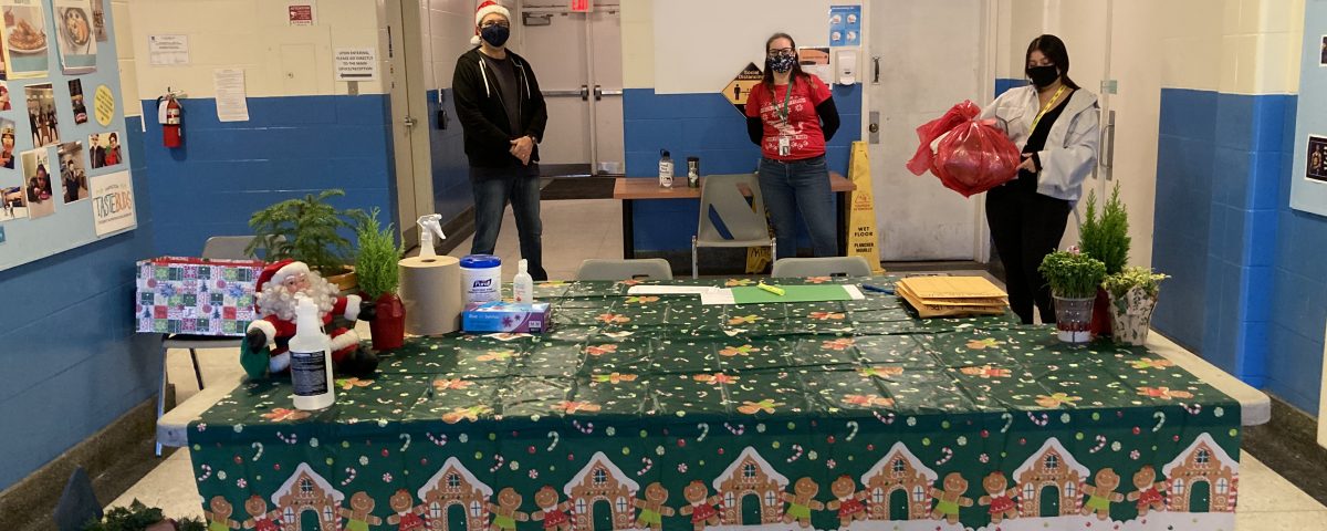 Three volunteers wearing masks stand behind a table decorated with a festive table cloth.