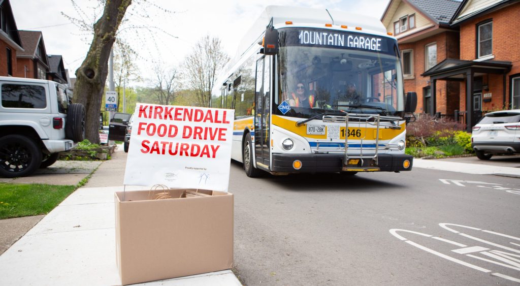 Kirkendall Food Drive sign behind box of donations with bus in the background